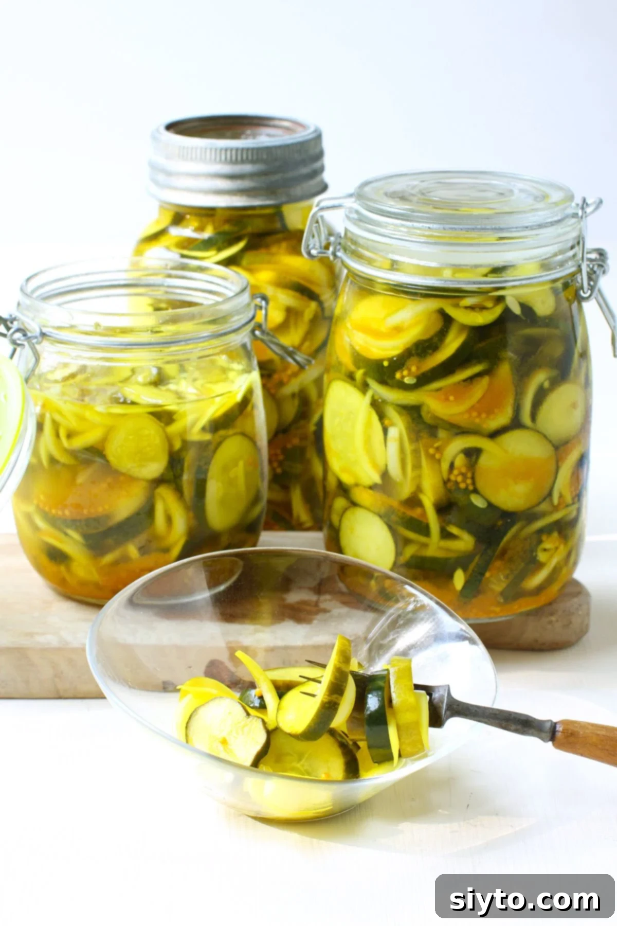 3 jars of refrigerator bread & butter pickles, with some in a small bowl in front and a fork holding some pickle slices, too.