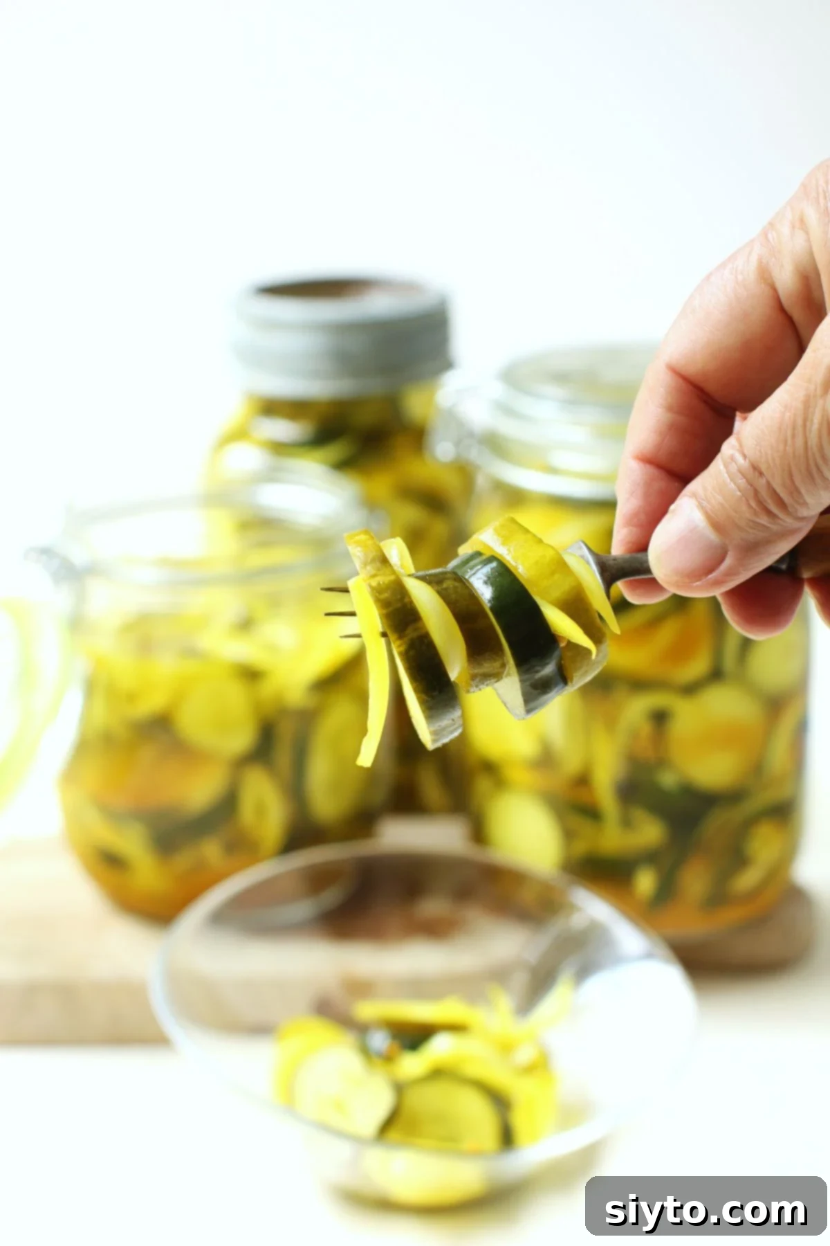 A forkful of pickle slices in front of the jars.