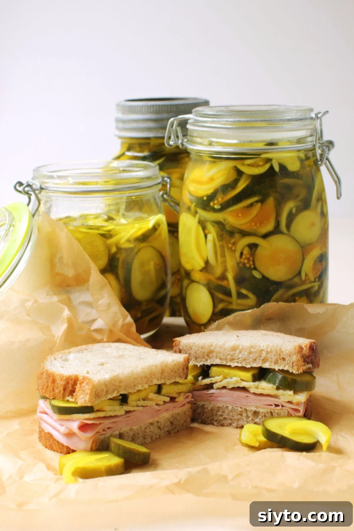 Jars of pickles and a cut open sandwich on brown paper in front of it.