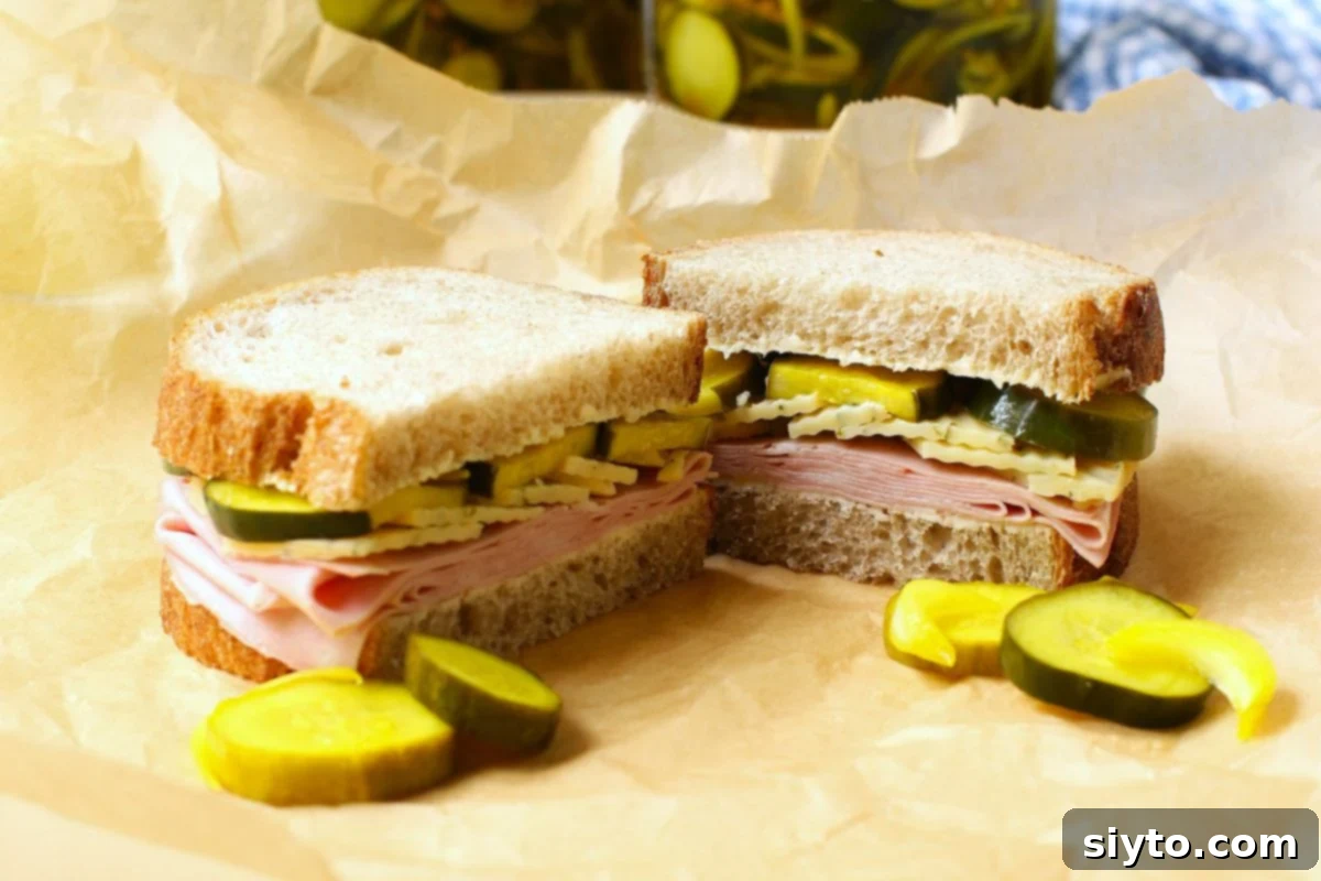 A rye bread sandwich with deli meat, cheese, and pickles on a brown paper wrapper.