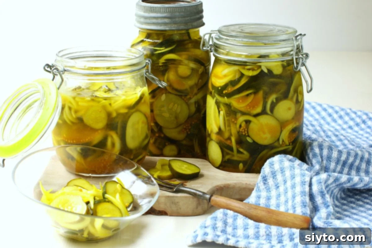 Horizontal photo of 3 jars refrigerator bread & butter pickles with some in a bowl, blue & white tea towel beside.