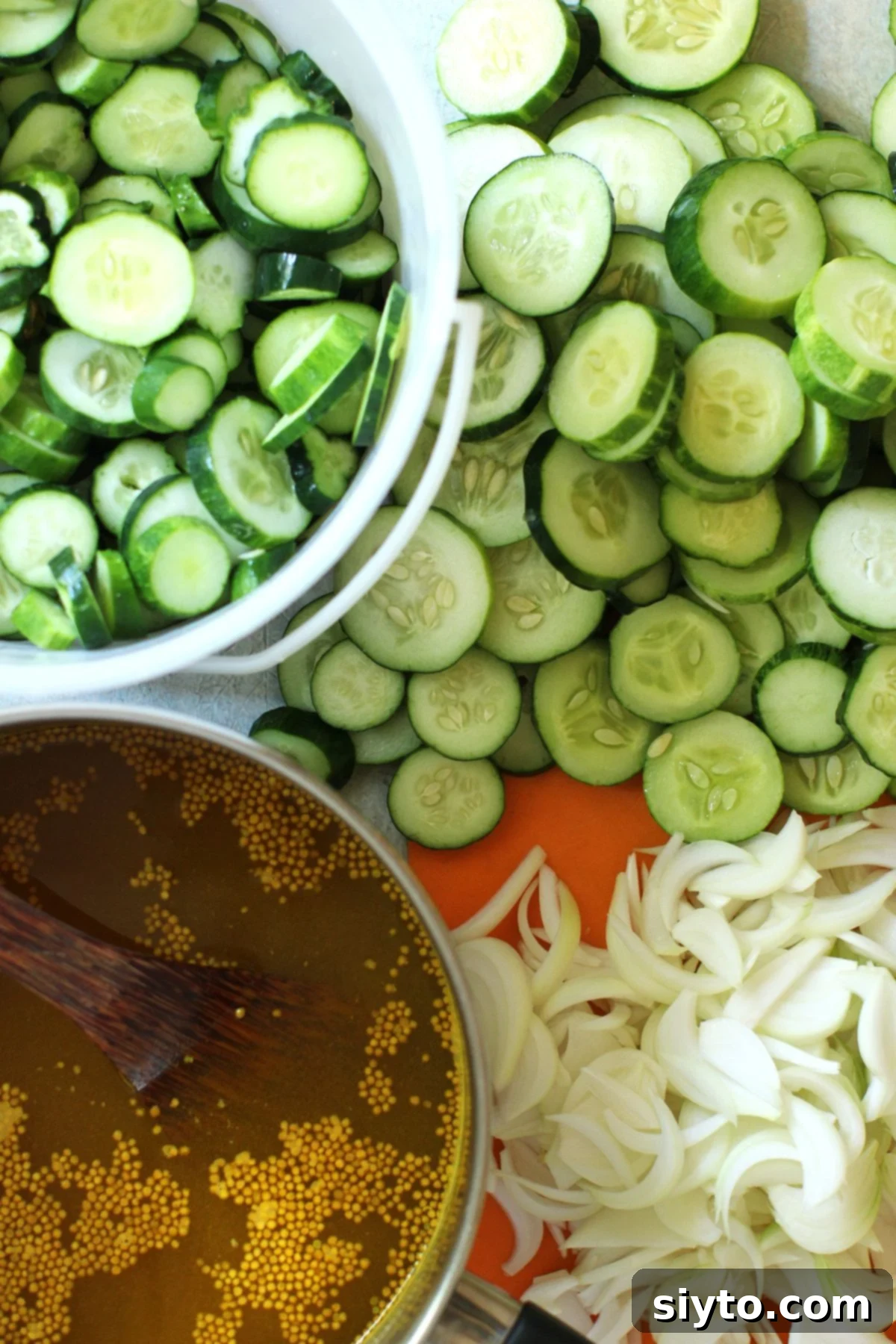 Piles of sliced cucumbers and onions and the cooked brine in a saucepan.