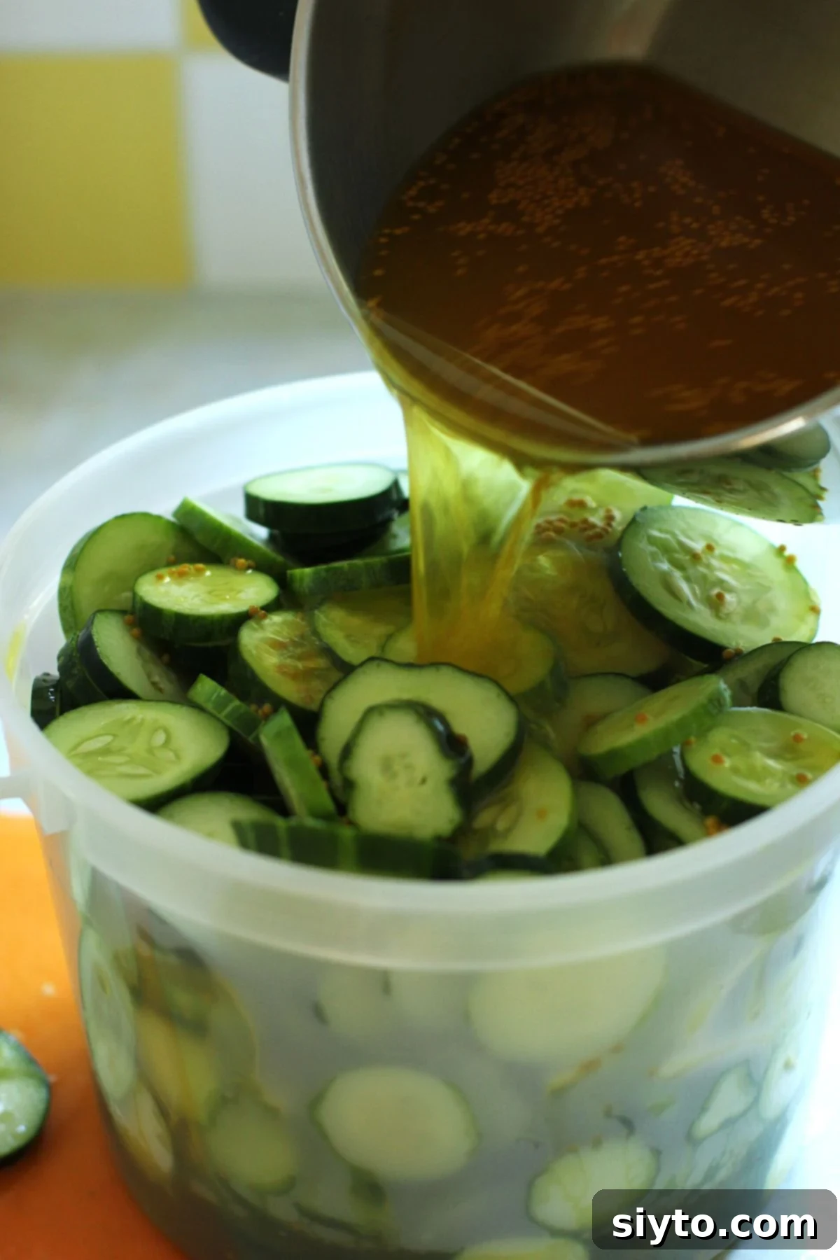 Pouring the brine over the sliced cucumbers in the pail.