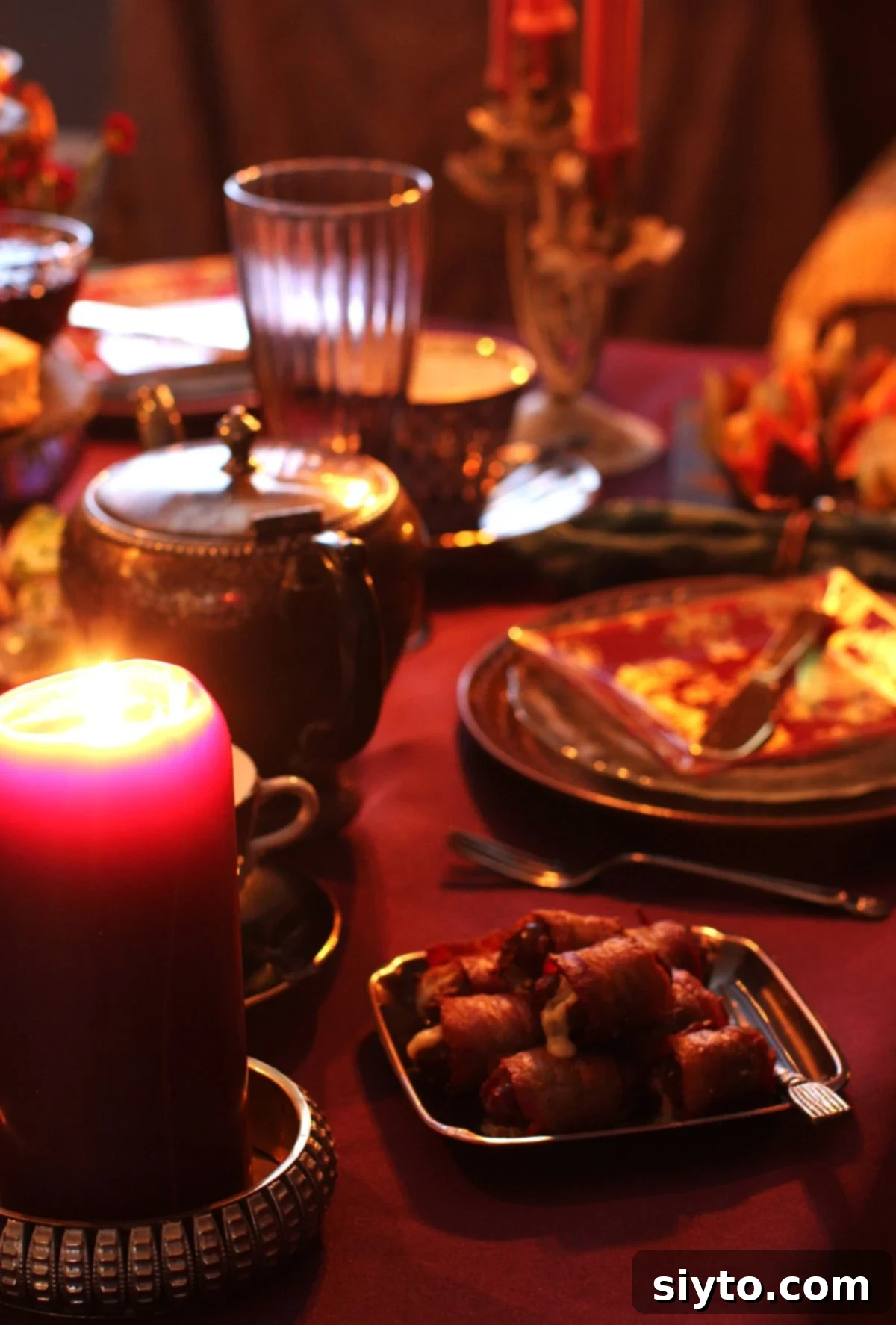 Dark tea table with candles, silver dishes, and a small plate of bacon wrapped dates.