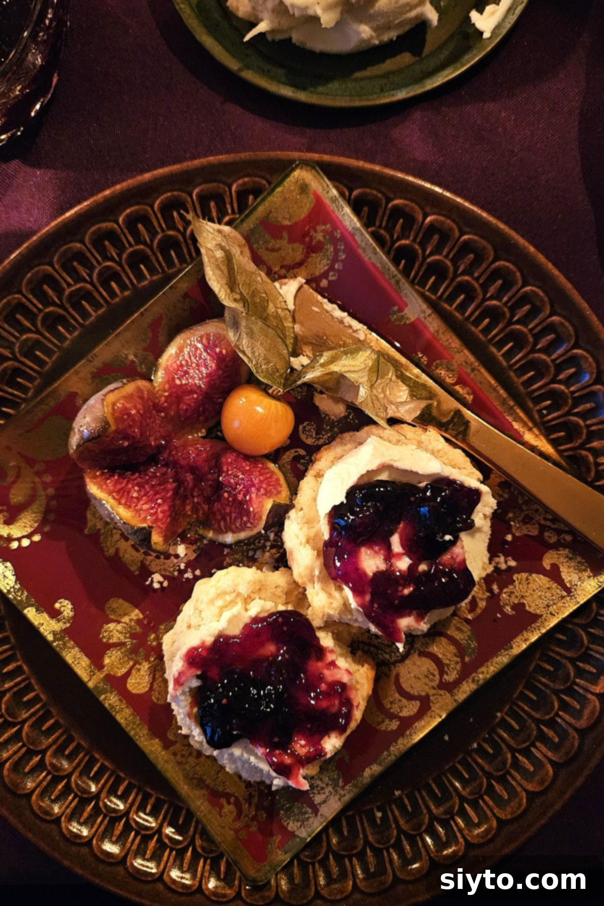 brown plate with scones spread with clotted cream and jam, fig, cape gooseberry.