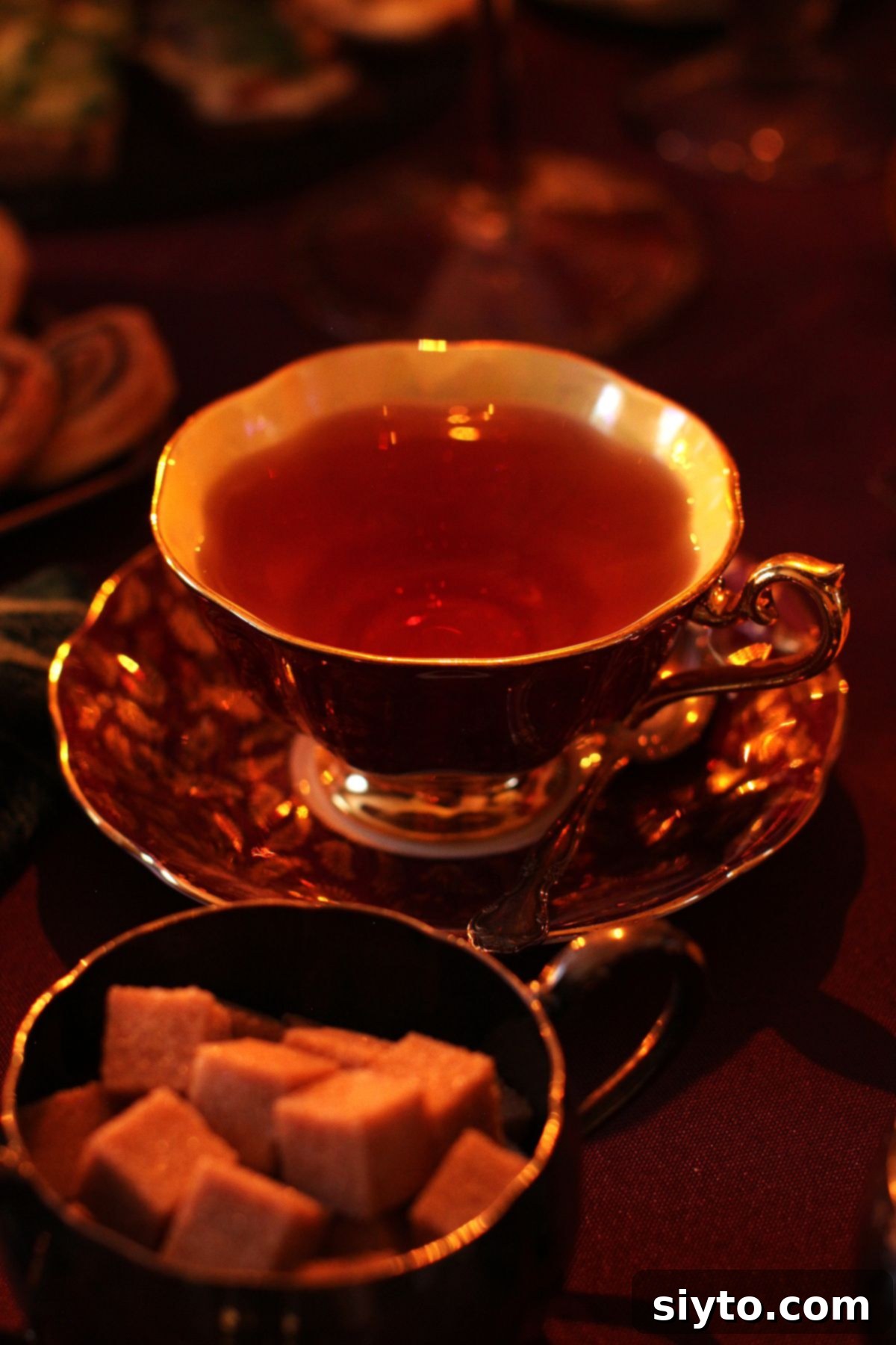 burgundy and gold china tea cup filled with tea, bowl of sugar cubes in front.
