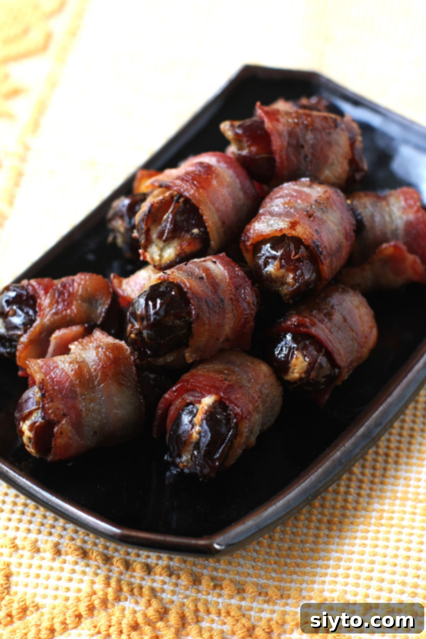 bacon wrapped dates on a rectangular black platter.