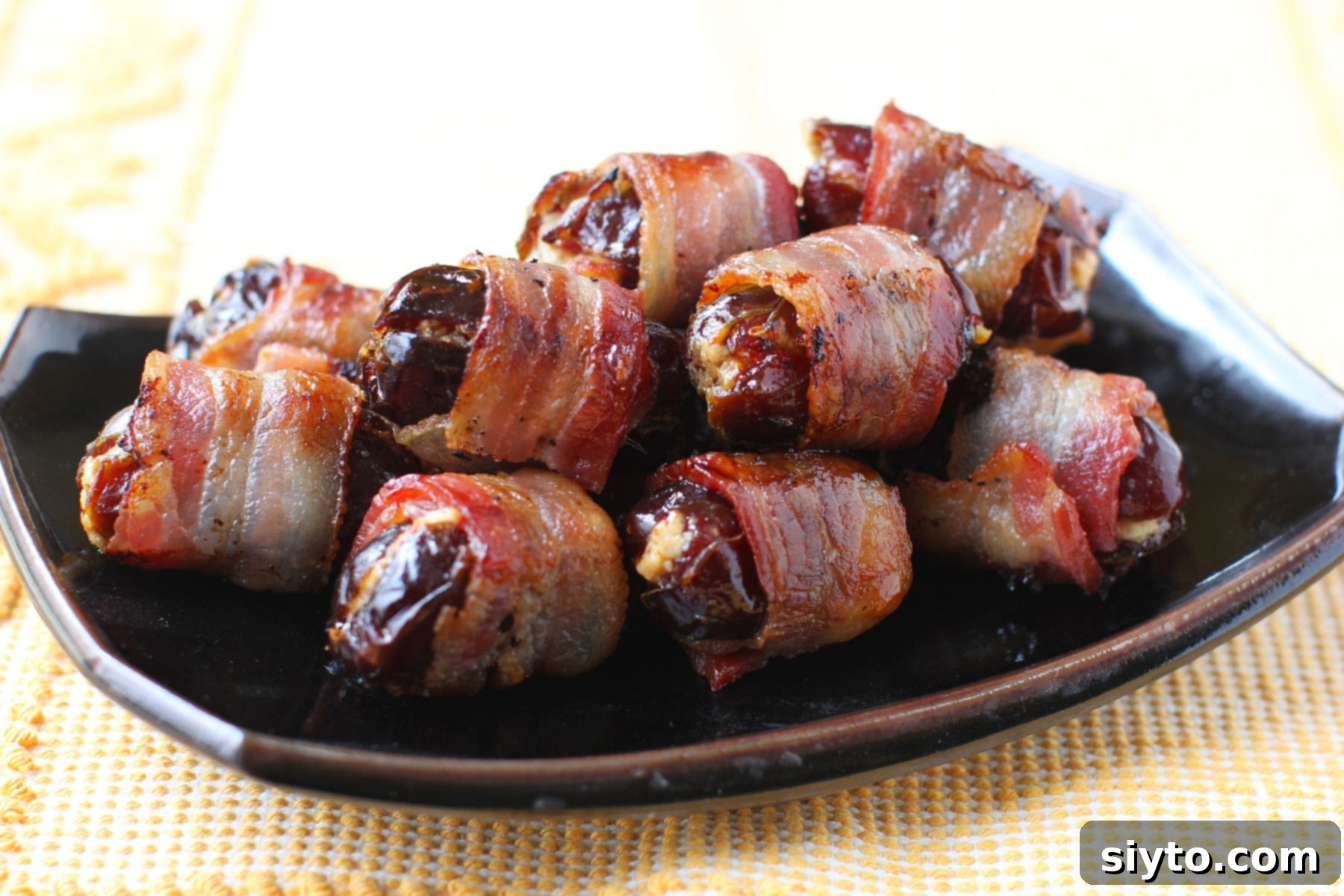 Black plate with a heap of bacon wrapped dates on it, on yellow mat.