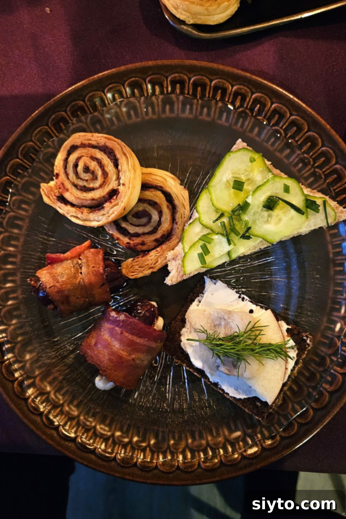 brown small plate of savouries, bacon wrapped dates, olive and anchovy spirals, cucumber sandwich, herring sandwich.